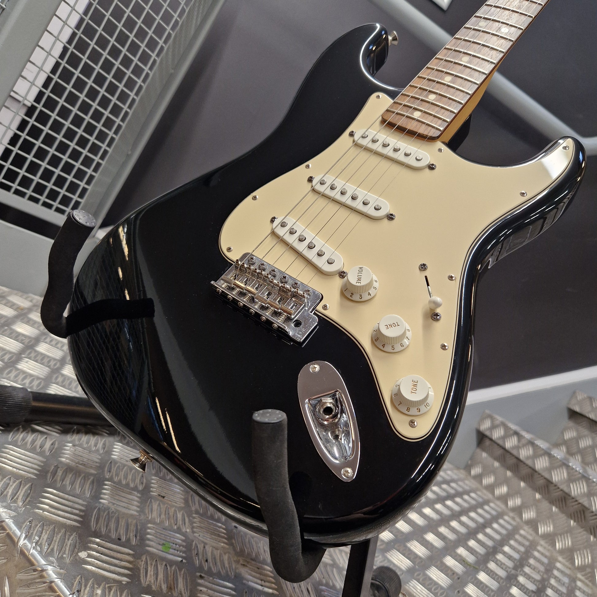 Pre-Owned Fender Standard Mexican Stratocaster 2011 Electric - Black A black electric guitar with a cream-colored pickguard and chrome hardware, resting on a metal stand.