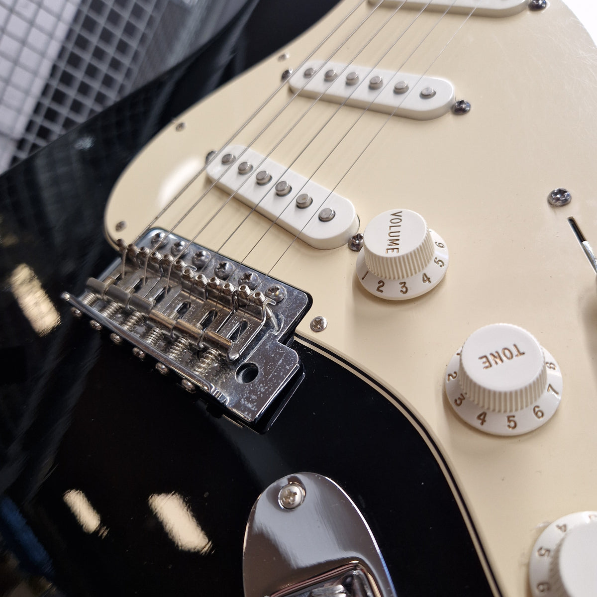 Pre-Owned Fender Standard Mexican Stratocaster 2011 Electric - Black Close-up of a black electric guitar body with a cream-colored pickguard, chrome hardware, and white control knobs labeled Volume and Tone.