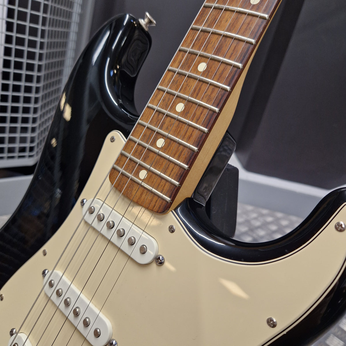 Pre-Owned Fender Standard Mexican Stratocaster 2011 Electric - Black Close-up of a black electric guitar with a cream-colored pickguard and a brown wood fretboard, resting on a stand.