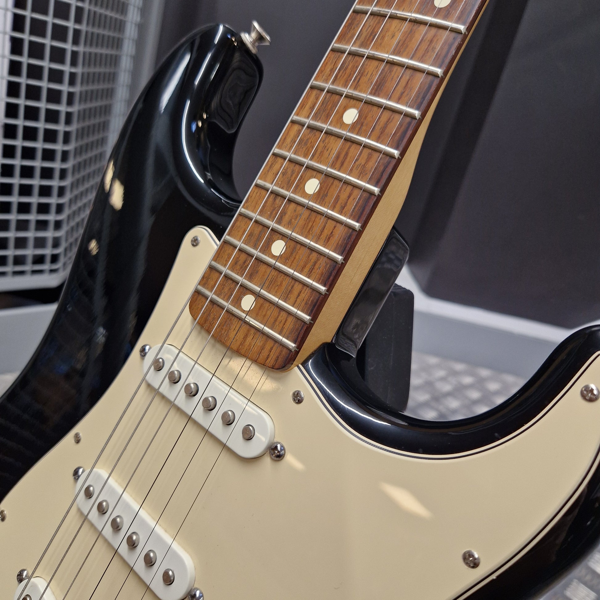 Pre-Owned Fender Standard Mexican Stratocaster 2011 Electric - Black Close-up of a black electric guitar with a cream-colored pickguard and a brown wood fretboard, resting on a stand.