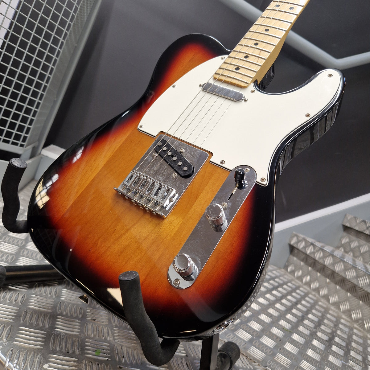 Pre-Owned Fender Player Telecaster 2022 Electric - 3-Colour Sunburst A classic electric guitar with a sunburst finish, resting on a metal stand in a workshop setting.