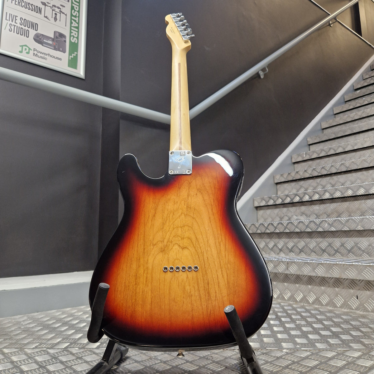Pre-Owned Fender Player Telecaster 2022 Electric - 3-Colour Sunburst A Fender Telecaster-style electric guitar shown from the back, resting on a stand in an indoor setting with a staircase and dark wall in the background.