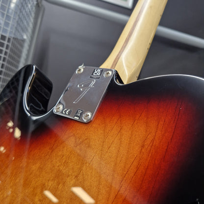 Pre-Owned Fender Player Telecaster 2022 Electric - 3-Colour Sunburst Close-up of the tailpiece and body of an electric guitar, showing a sunburst finish, a black pickguard, and a silver metal plate with a stylized 'F' logo. The neck is a light natural wood color.