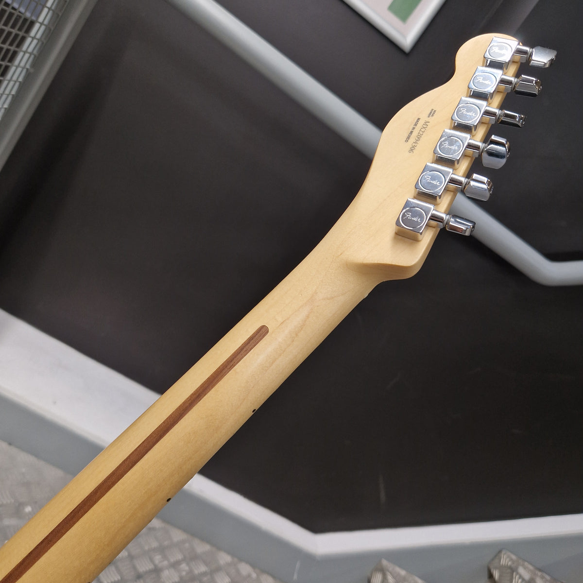 Pre-Owned Fender Player Telecaster 2022 Electric - 3-Colour Sunburst Close-up of the headstock and neck of an electric guitar, showing a natural light wood finish, a brown inlay stripe, and silver tuning pegs against a dark gray background.