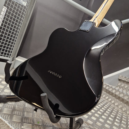 Pre-Owned Harley Benton JA-Baritone HH Electric - Black Close-up of the glossy black back of an electric guitar body on a stand, with part of the light wood neck visible and a dark gray indoor background.