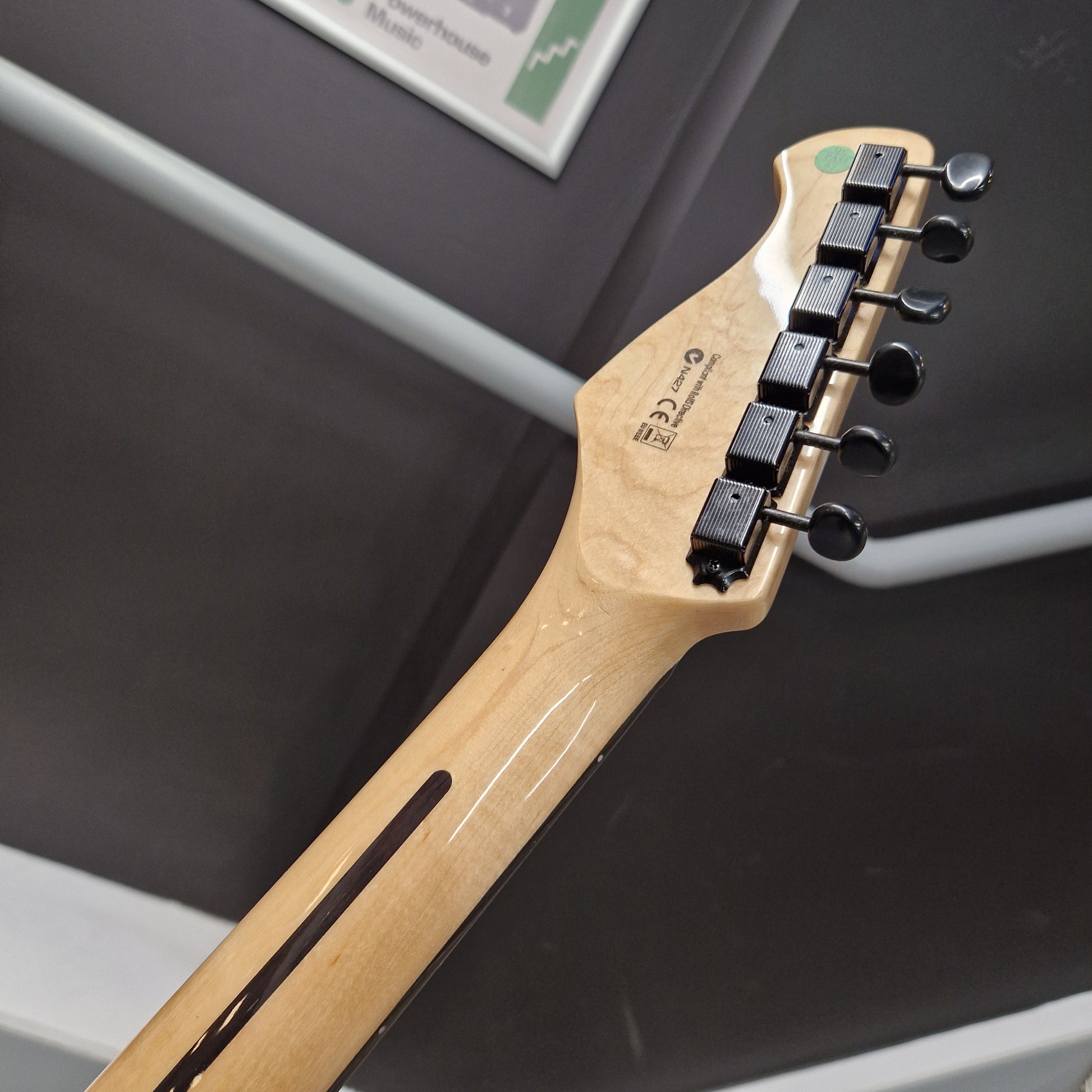 Pre-Owned Harley Benton JA-Baritone HH Electric - Black  Close-up of the headstock of a guitar with a natural light wood finish and black tuning pegs, photographed indoors against a dark gray background.