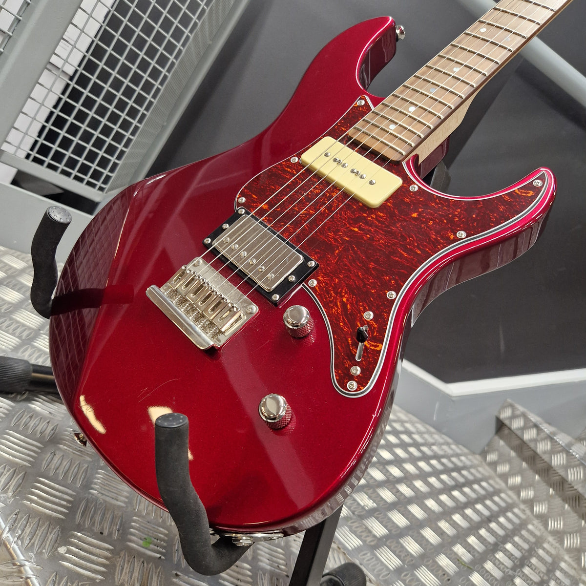 Pre-Owned Yamaha Pacifica 311H Electric - Red Metallic A red electric guitar with a glossy red body, tortoiseshell pickguard, and gold humbucker pickups, resting on a metal stand.