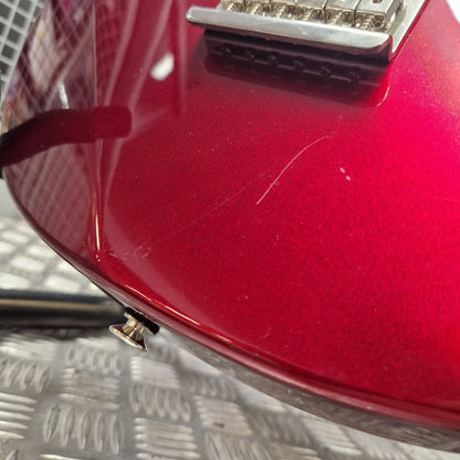 Pre-Owned Yamaha Pacifica 311H Electric - Red Metallic Close-up of a glossy red electric guitar body showing a chrome bridge, a small silver control knob, and some surface scratches on the finish, set against a textured gray metal surface.