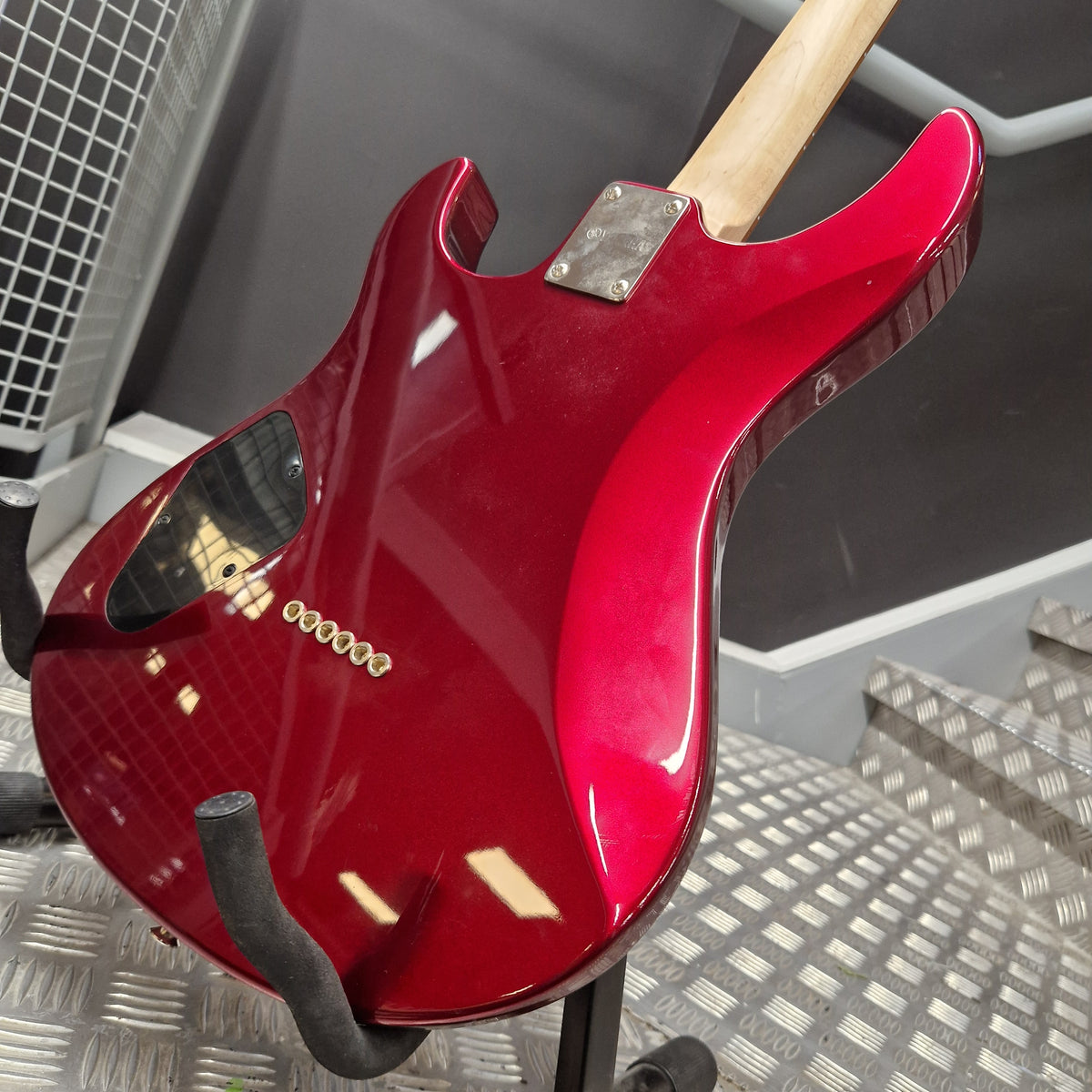 Pre-Owned Yamaha Pacifica 311H Electric - Red Metallic A glossy red electric guitar body shown from the back, mounted on a stand in a workshop or studio setting with a metal diamond-plate floor and dark background.