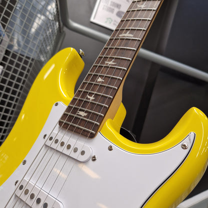 Pre-Owned PRS SE Silver Sky John Mayer Signature Electric - Dandy Lion Close-up of a bright yellow electric guitar body with a white pickguard and dark brown fretboard, photographed indoors against a gray metal structure.