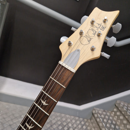 Pre-Owned PRS SE Silver Sky John Mayer Signature Electric - Dandy Lion Close-up of an acoustic guitar headstock and upper neck, showing a light natural wood headstock with six white tuning pegs and a dark brown fretboard with inlays, photographed indoors against a dark wall and metal steps.