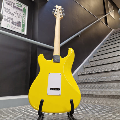 Pre-Owned PRS SE Silver Sky John Mayer Signature Electric - Dandy Lion A bright yellow electric guitar body on a stand, photographed indoors against a dark wall with a staircase and metal handrail in the background.