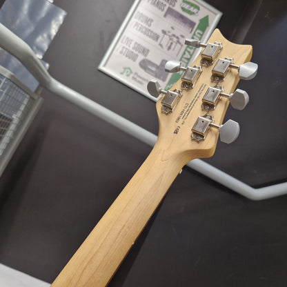 Pre-Owned PRS SE Silver Sky John Mayer Signature Electric - Dandy Lion Close-up of the headstock of a guitar with a natural wood finish and six silver tuning pegs, photographed indoors against a dark wall with a framed poster in the background.