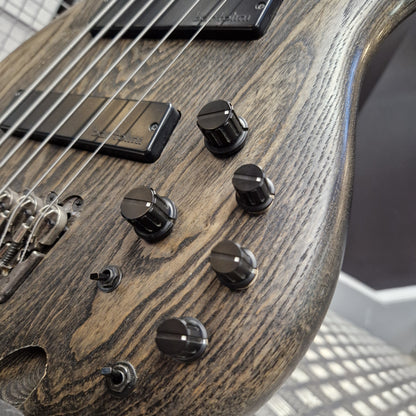 Pre-Owned Ibanez SRFF806 Multi-Scale 6-String Bass - Black Stained Close-up of a bass guitar body showing the wood grain finish, black control knobs, pickups, and strings.