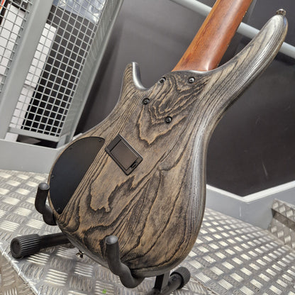 Pre-Owned Ibanez SRFF806 Multi-Scale 6-String Bass - Black Stained Close-up of the back of an electric guitar showing a distressed dark wood grain finish, resting on a black stand over a diamond plate metal surface.