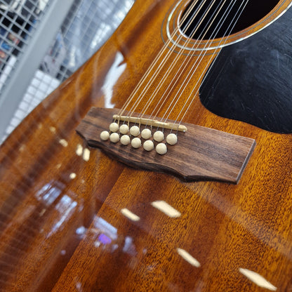 Pre-Owned Guild D-125-12NAT Dreadnought 12-String Acoustic - Mahogany Close-up of an acoustic guitar body showing the glossy brown wood finish, bridge with cream-colored tuners, and part of the black pickguard, with a blurred outdoor background.