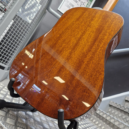 Pre-Owned Guild D-125-12NAT Dreadnought 12-String Acoustic - Mahogany Close-up of the back of a wooden acoustic guitar on a stand, showing a glossy warm brown wood finish with visible grain and reflections.