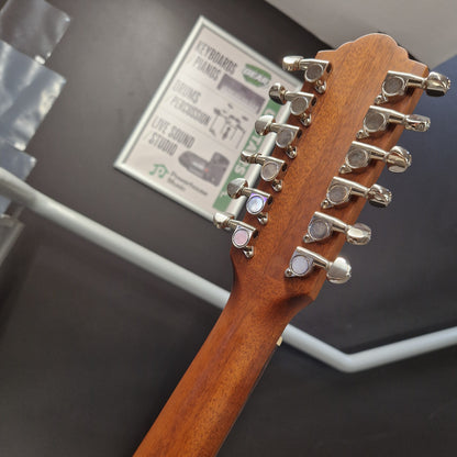 Pre-Owned Guild D-125-12NAT Dreadnought 12-String Acoustic - Mahogany Close-up of the headstock of a wooden twelve-string guitar, showing the side tuners with silver and pink accents, set against a dark wall with a piano store sign in the background.