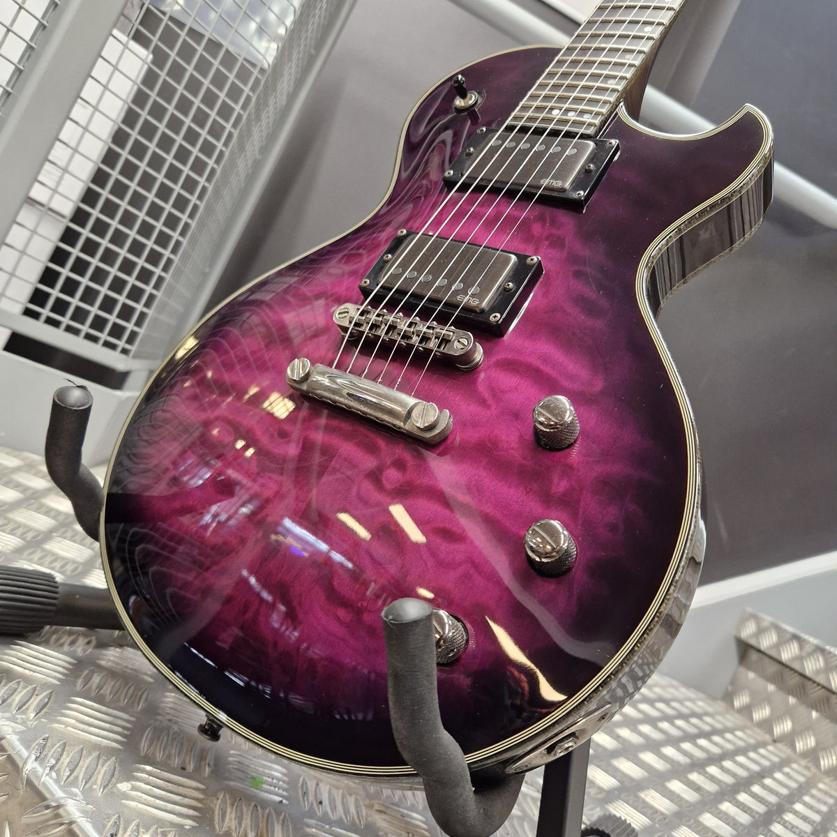 Pre-Owned Schecter Hellraiser Hybrid Solo-II Electric - Transparent Purple Burst A purple and magenta flame-glazed electric guitar with chrome hardware, resting on a black stand on a metal diamond plate floor.