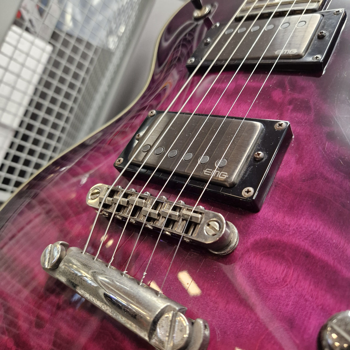 Pre-Owned Schecter Hellraiser Hybrid Solo-II Electric - Transparent Purple Burst Close-up of a purple electric guitar body with black humbucker pickups and chrome hardware, photographed indoors against a blurred metal grid background.