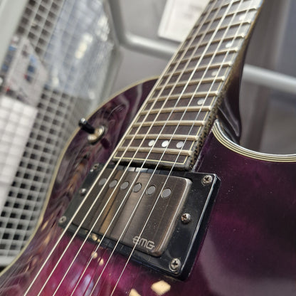 Pre-Owned Schecter Hellraiser Hybrid Solo-II Electric - Transparent Purple Burst Close-up of a purple humbucker electric guitar body and neck, featuring a black AMG pickup cover and gold truss rod cover, with a blurred store background.
