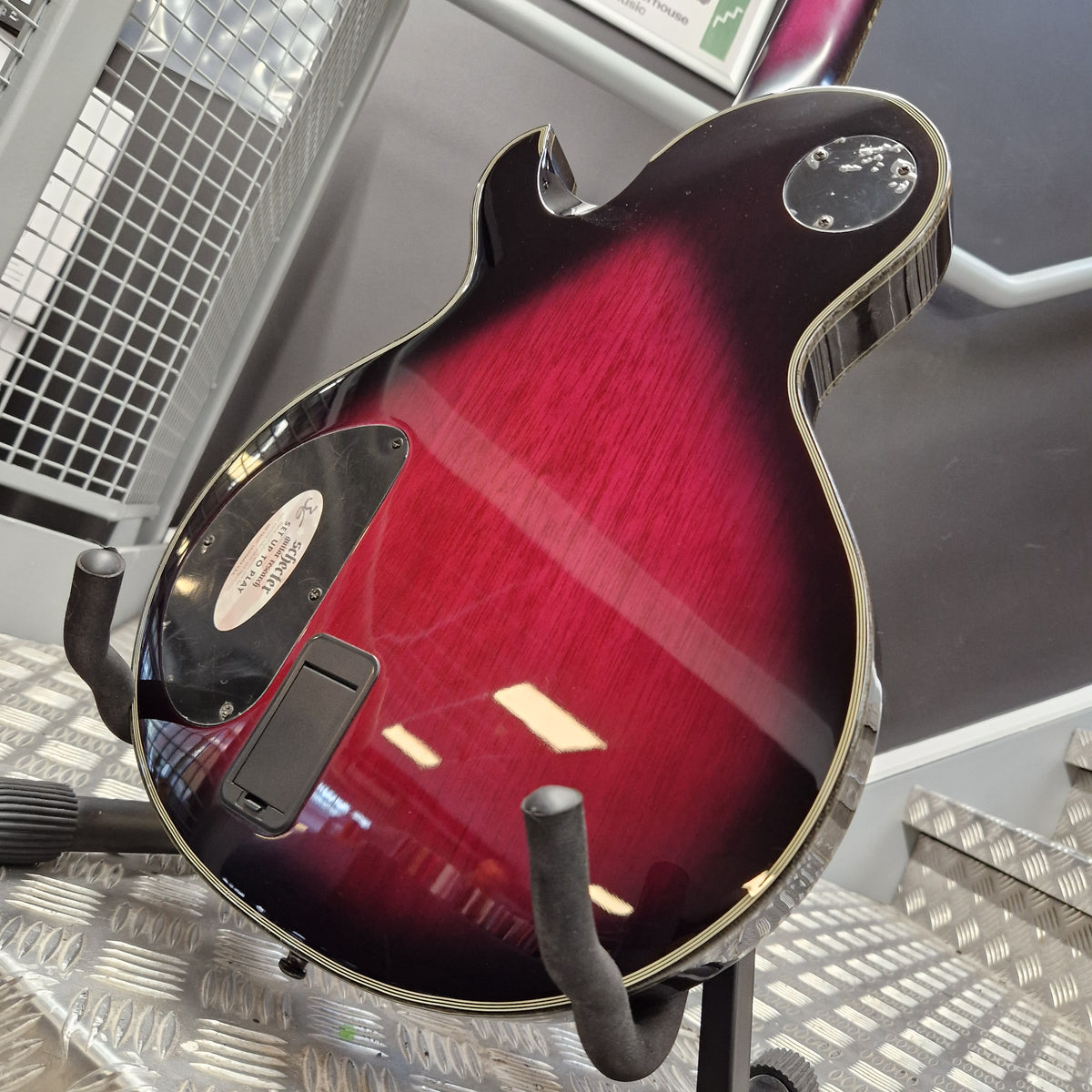 Pre-Owned Schecter Hellraiser Hybrid Solo-II Electric - Transparent Purple Burst Close-up of the back of an electric guitar body in a dark red to black sunburst finish, mounted on a stand in a shop setting.