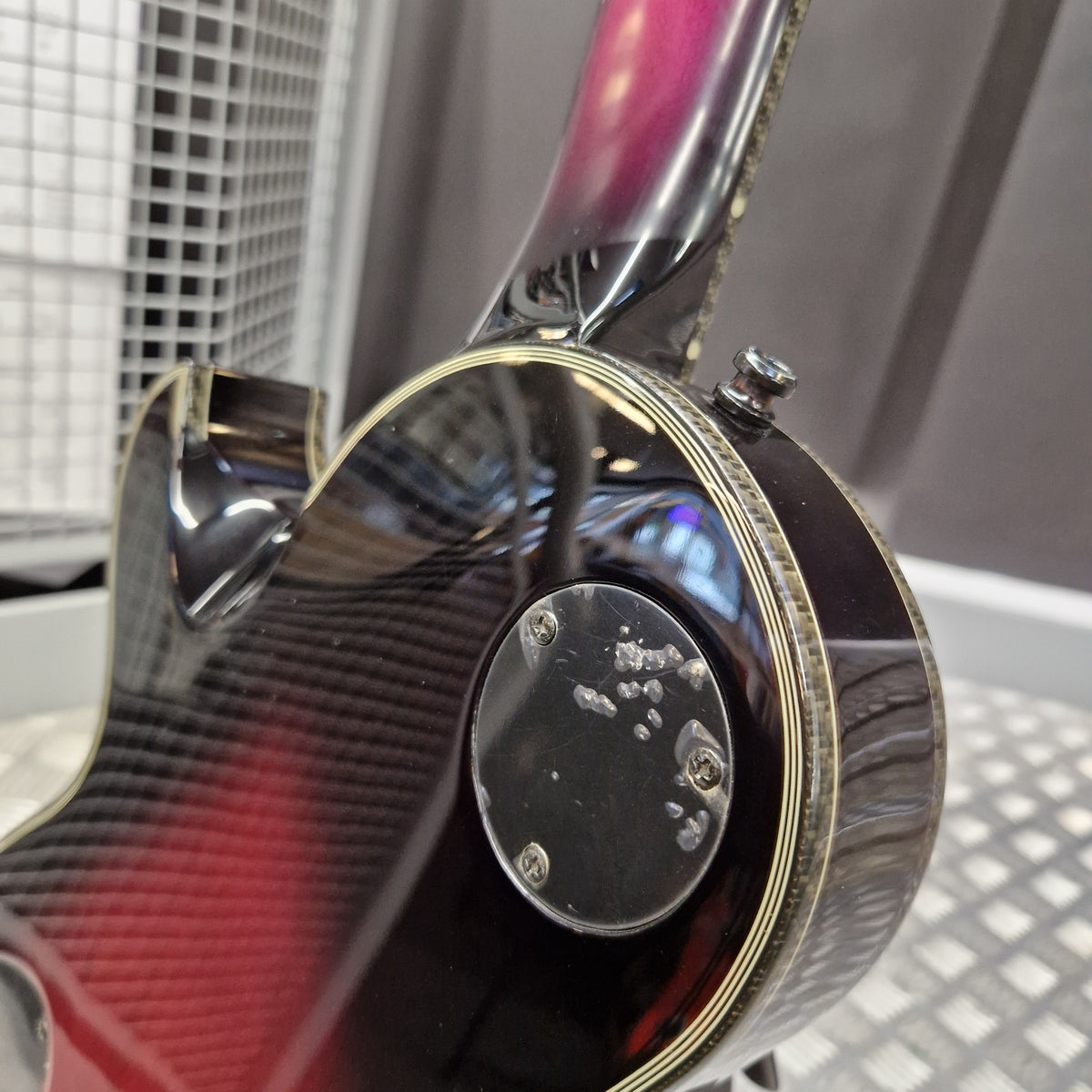 Pre-Owned Schecter Hellraiser Hybrid Solo-II Electric - Transparent Purple Burst Close-up of the rear body of an electric guitar with a glossy black carbon fiber pattern finish, gold trim, and a pinkish-purple neck visible in the background.