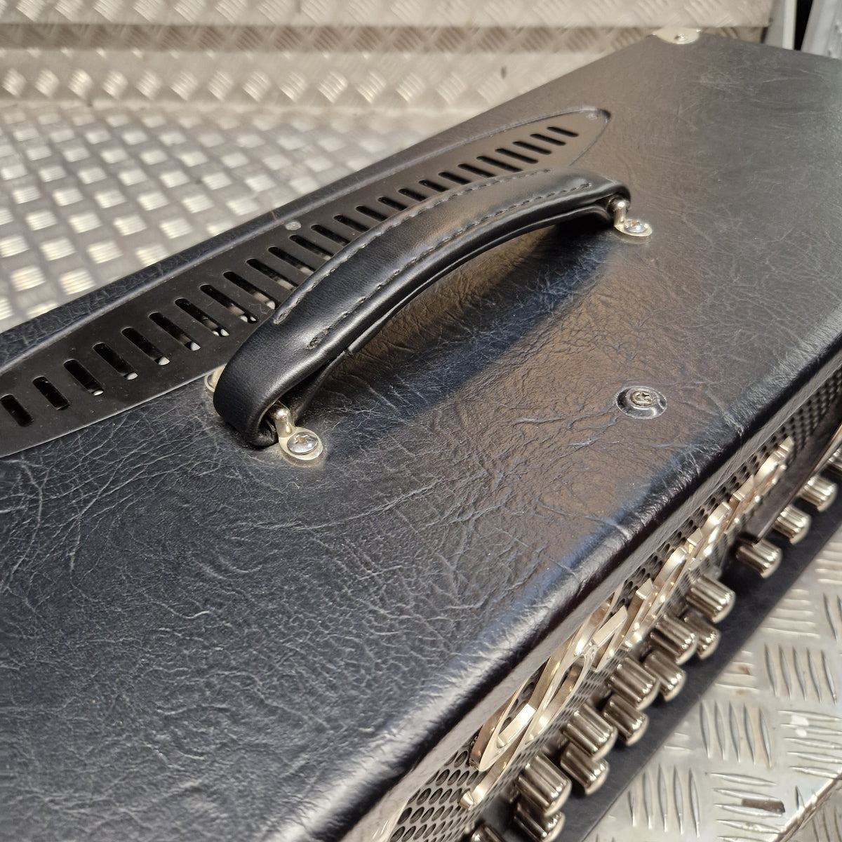 Pre-Owned Bugera 333XL Infinium 120w Electric Amplifer Head Close-up of a black textured leather guitar amplifier handle with silver metal hardware, set against a diamond plate metal background.