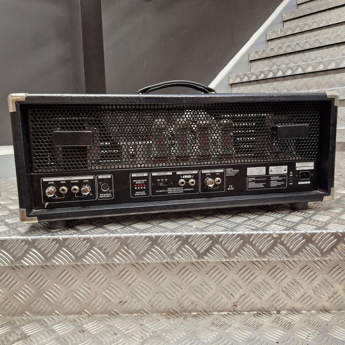 Pre-Owned Bugera 333XL Infinium 120w Electric Amplifer Head A black Fender guitar amplifier head with a metal mesh front grille and control panel, resting on a diamond plate metal staircase.