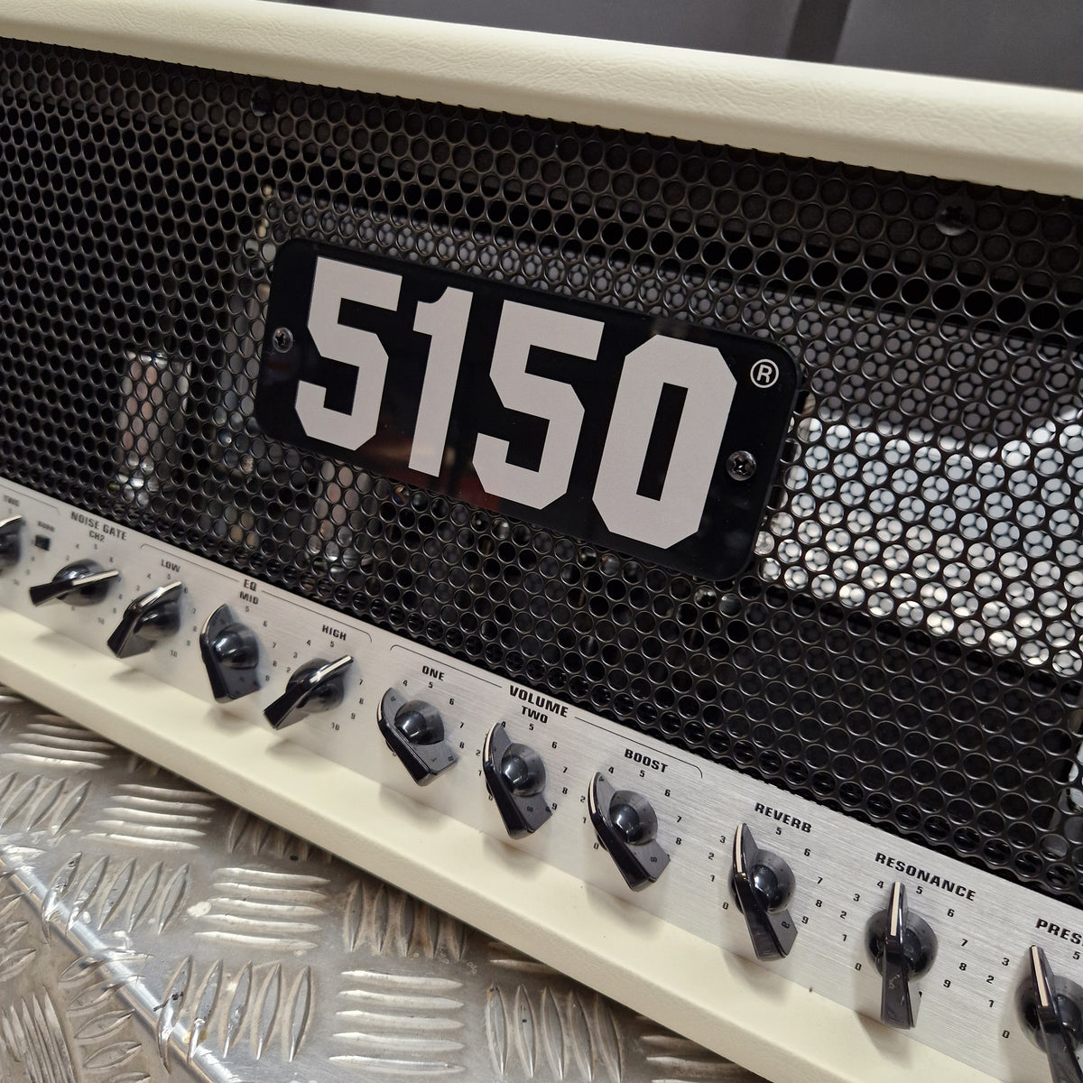 Pre-Owned EVH 5150 Iconic 80W Electric Amplifier Head Close-up of a 5150 guitar amplifier head with a cream-colored faceplate, black mesh grille, and black control knobs on a silver diamond plate floor.