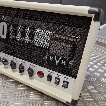 Pre-Owned EVH 5150 Iconic 80W Electric Amplifier Head Close-up of an EVH guitar amplifier head with cream-colored leatherette corners and front panel, black honeycomb grille, control knobs, and power switches, resting on a diamond plate metal surface.