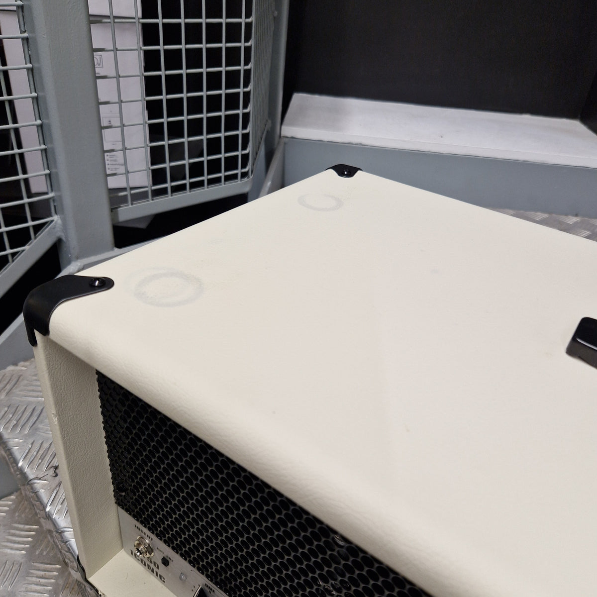 Pre-Owned EVH 5150 Iconic 80W Electric Amplifier Head A close-up of a cream-colored guitar amplifier or speaker cabinet corner, showing black corner protectors and a black front grille, set against a dark background.