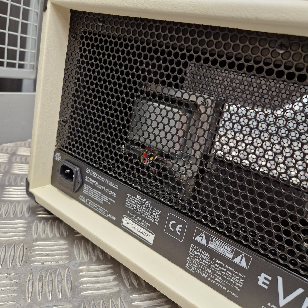 Pre-Owned EVH 5150 Iconic 80W Electric Amplifier Head Close-up of the rear panel of a cream-colored guitar amplifier, showing the black honeycomb grille, power input jack, and regulatory labels on a diamond plate metal surface.