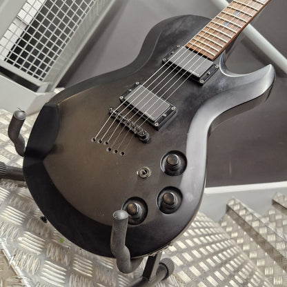 Pre-Owned Cort EVL-Z4 Electric - Satin Black A close-up of a black electric guitar body with dual humbucker pickups, three control knobs, and a dark fretboard, resting on a metal stand.