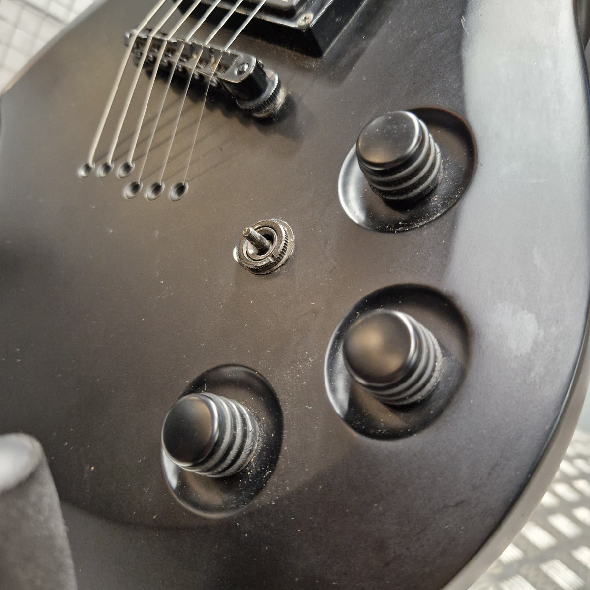 Pre-Owned Cort EVL-Z4 Electric - Satin Black Close-up of the lower bout body of a black electric guitar, showing the three control knobs, a silver toggle switch, and part of the bridge and strings.