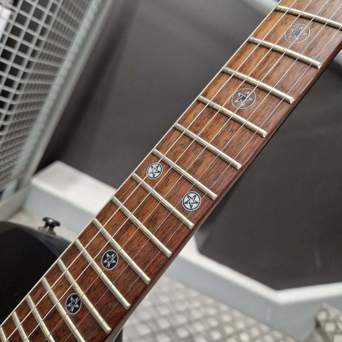 Pre-Owned Cort EVL-Z4 Electric - Satin Black Close-up of a guitar fretboard with dark brown wood, silver metal frets, and circular black inlays, photographed against a gray and white background.