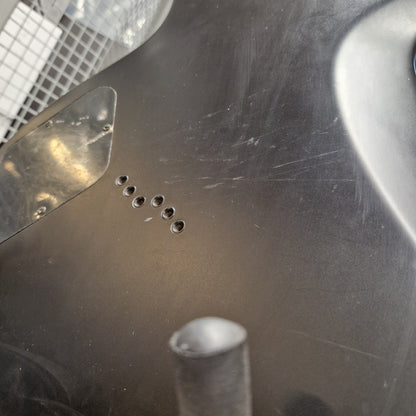 Pre-Owned Cort EVL-Z4 Electric - Satin Black Close-up of a dark metallic surface with a series of five small circular holes and a reflective brushed metal texture.