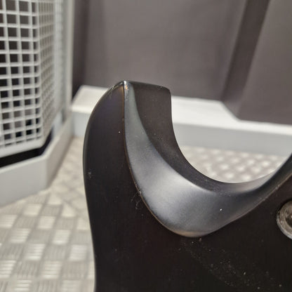Pre-Owned Cort EVL-Z4 Electric - Satin Black Close-up of a black curved plastic component, likely a handle or bracket, showing a worn or scratched edge against a gray and white industrial background.