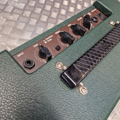 Pre-Owned Vox Pathfinder 10 Electric Amplifier Combo Close-up of a green textured amplifier head with black control knobs, a black handle, and a brown control panel, photographed against a metal diamond-plate floor.