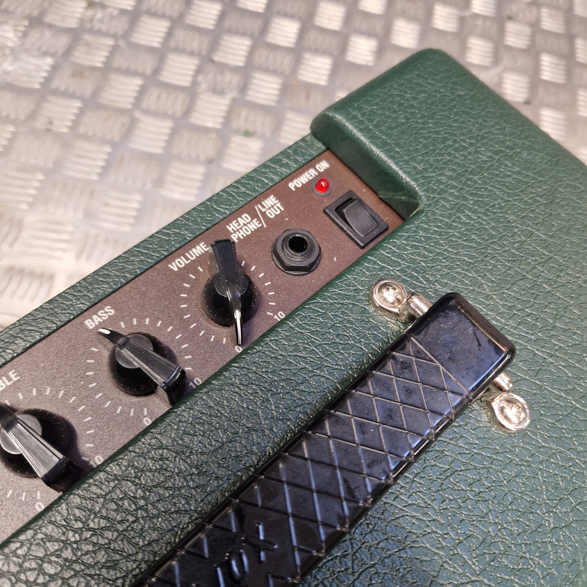 Pre-Owned Vox Pathfinder 10 Electric Amplifier Combo Close-up of a green textured amplifier head with a black control panel, knobs, and a black foot pedal on a metal grate background.