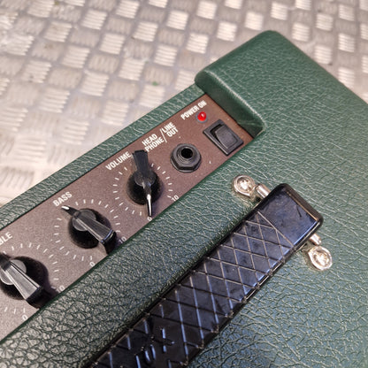 Pre-Owned Vox Pathfinder 10 Electric Amplifier Combo Close-up of a green textured amplifier head with a black control panel, knobs, and a black foot pedal on a metal grate background.