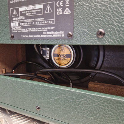 Pre-Owned Vox Pathfinder 10 Electric Amplifier Combo Close-up of a green textured speaker cabinet showing a round black and gold VOX speaker inside, with black cables and a black specification label on the left.