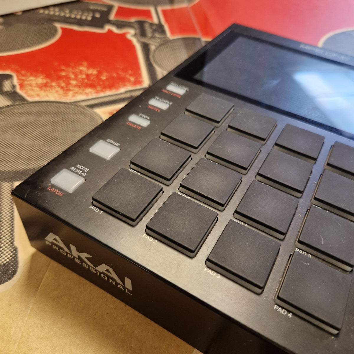 Pre-Owned Akai MPC ONE Standalone Music Production Centre A close-up angled view of a black Akai Professional 16-pad electronic drum pad controller, showing the side screen, touch pads, and white brand logo on a cardboard surface.
