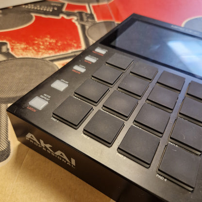 Pre-Owned Akai MPC ONE Standalone Music Production Centre A close-up angled view of a black Akai Professional 16-pad electronic drum pad controller, showing the side screen, touch pads, and white brand logo on a cardboard surface.