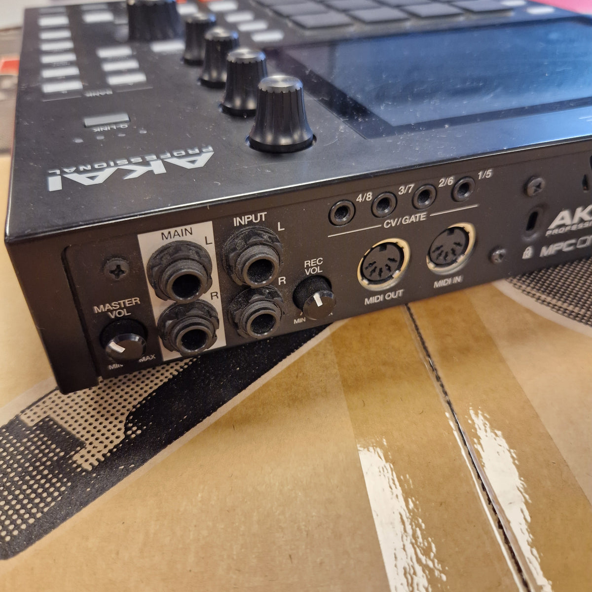 Pre-Owned Akai MPC ONE Standalone Music Production Centre Close-up of the rear panel of an Akai DMX512 controller, showing input and output jacks, knobs, and labels, resting on a cardboard box.