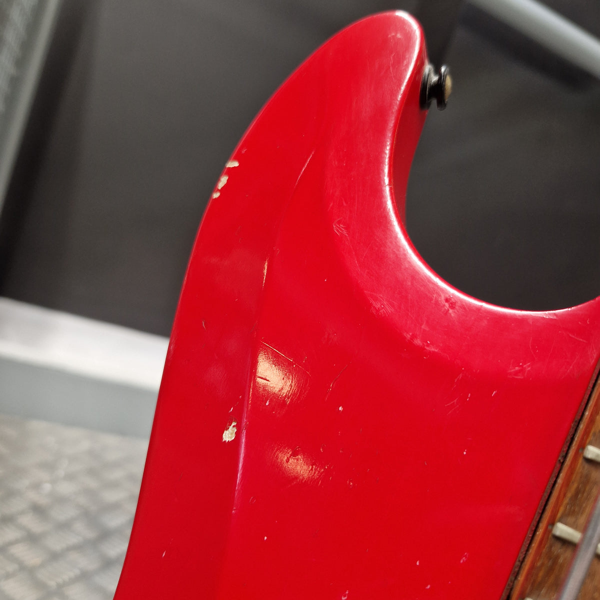Pre-Owned Hagstrom Futurama Deluxe 1960s Bass - Red Close-up of a red electric guitar body showing the lower bout curve, a small black hardware screw, and part of a wooden fretboard.