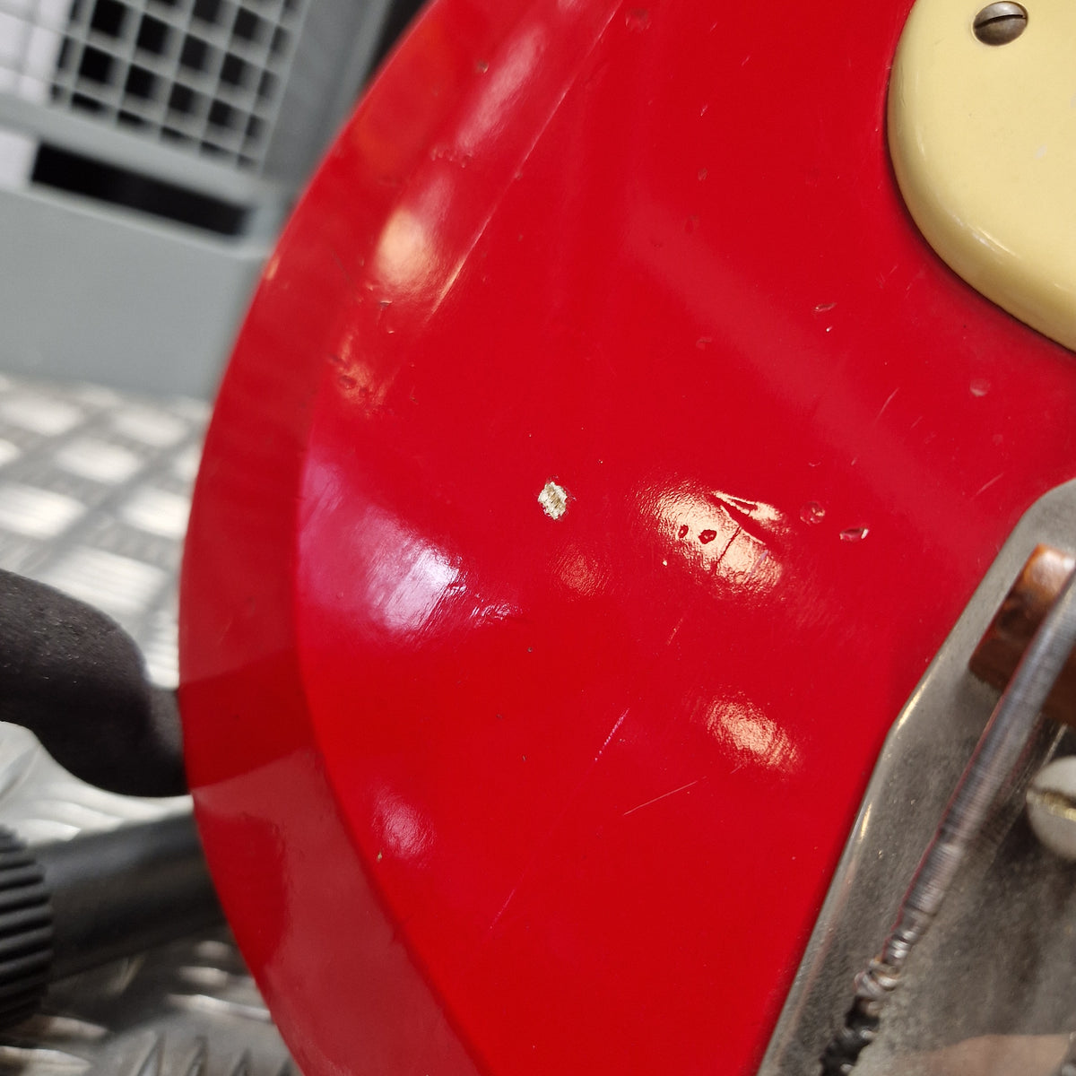 Pre-Owned Hagstrom Futurama Deluxe 1960s Bass - Red Close-up of a glossy red electric guitar body with a cream-colored headstock edge and metal hardware visible at the top, photographed indoors with some reflections and surface wear.