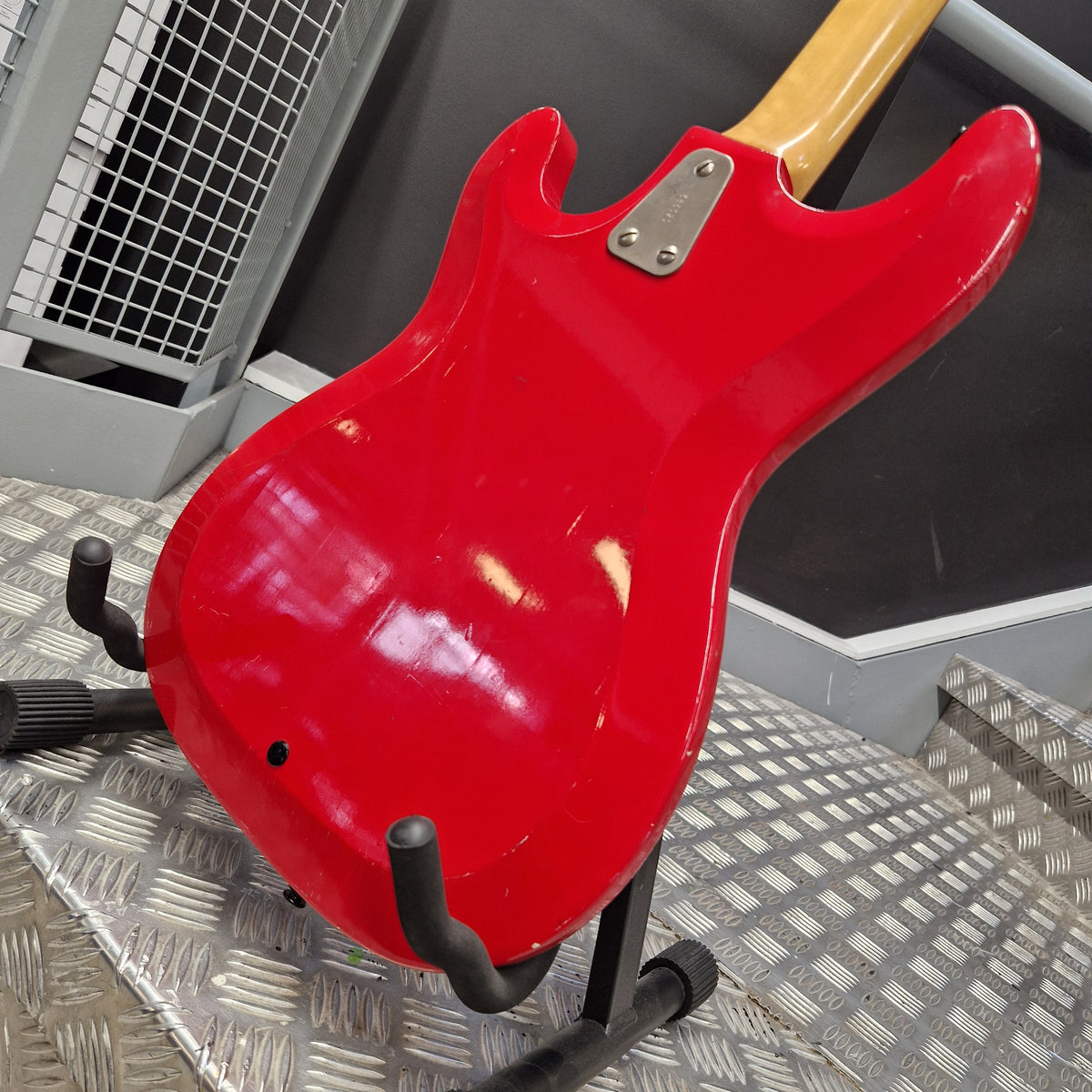 Pre-Owned Hagstrom Futurama Deluxe 1960s Bass - Red A red electric guitar body shown from the back, resting on a black stand on a diamond plate metal floor.