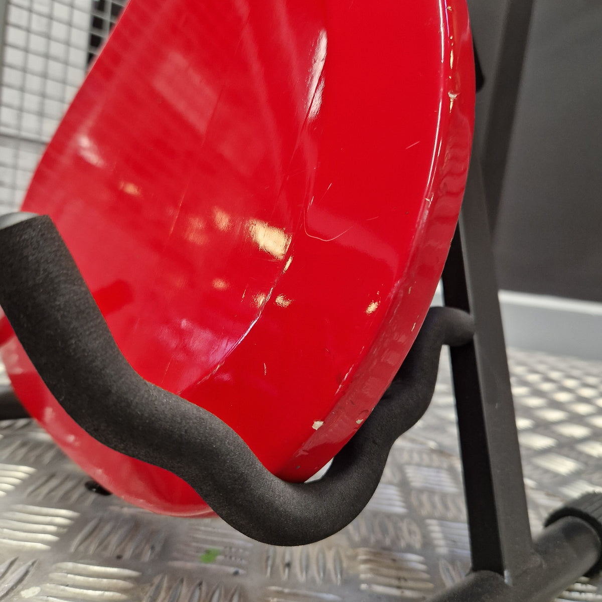 Pre-Owned Hagstrom Futurama Deluxe 1960s Bass - Red A close-up of a red plastic sled or scoop with a black foam handle, resting against a textured silver metal wall.