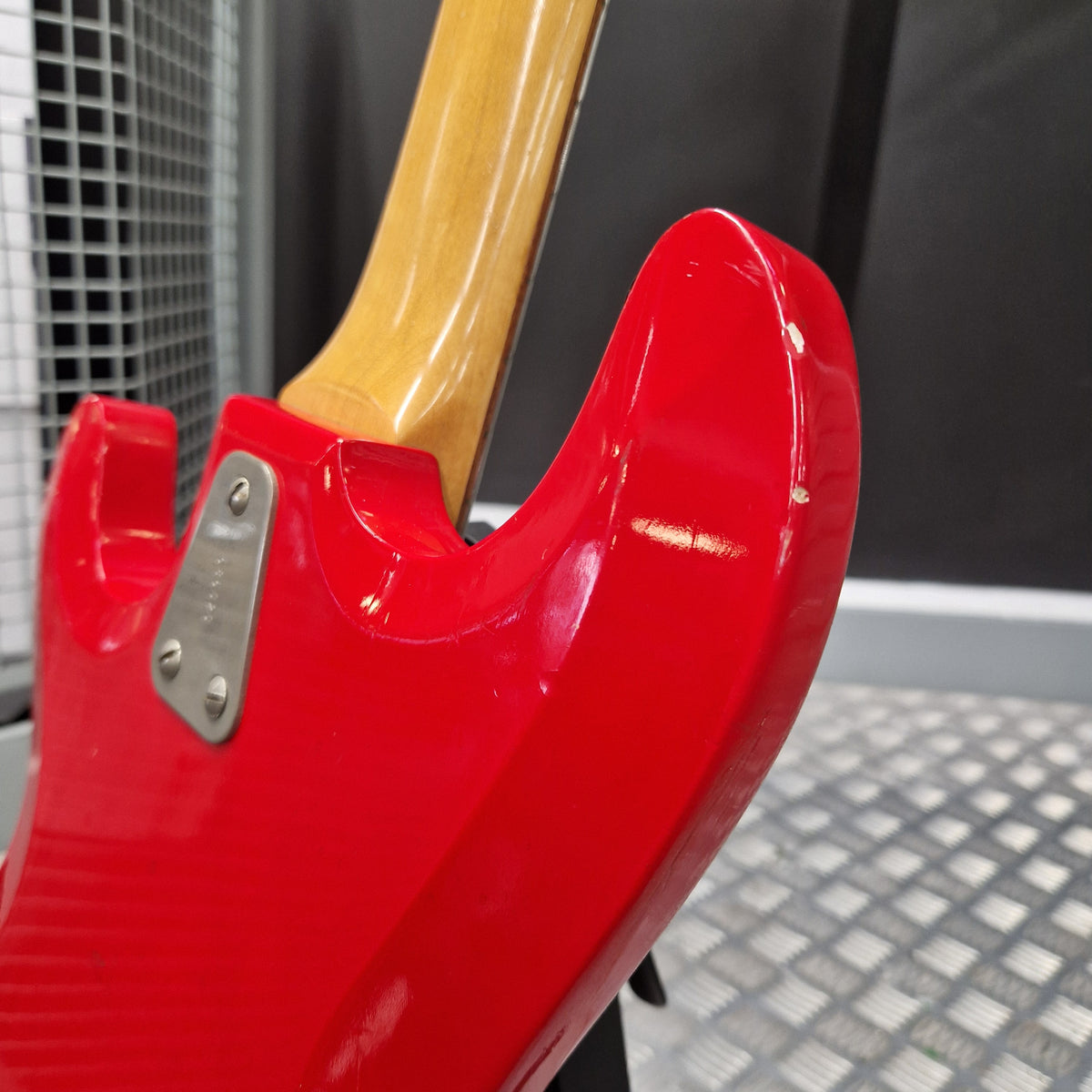 Pre-Owned Hagstrom Futurama Deluxe 1960s Bass - Red Close-up of the rear side of a glossy red electric guitar body with a light wood neck and a metal hardware plate, photographed indoors against a dark and gray background.